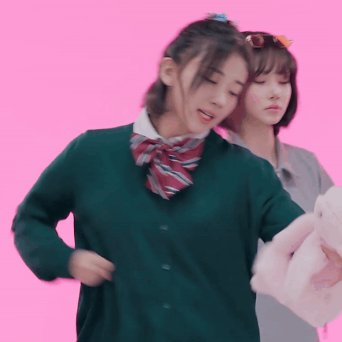 A Girl In A Green Sweater Is Standing Next To Another Girl In A Grey Shirt GIF