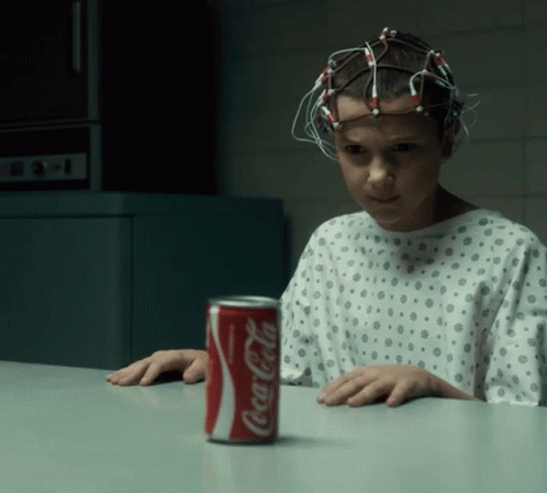 A Girl In A Hospital Gown Sits At A Table With A Can Of Coca Cola On It GIF