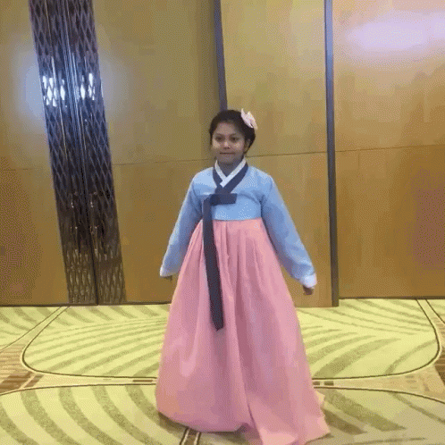 A Girl In A Pink And Blue Dress Is Standing On A Rug GIF