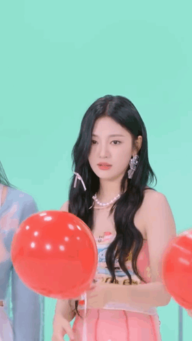 A Girl In A Pink Dress Is Holding A Red Balloon In Front Of Her Face . GIF