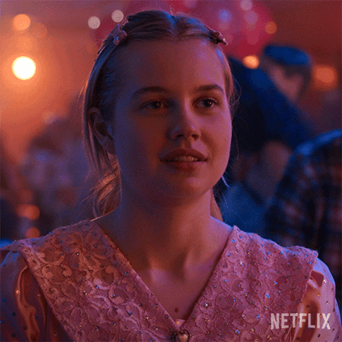 A Girl In A Pink Dress Is Sitting In A Room With A Netflix Logo On The Bottom Right Corner . GIF