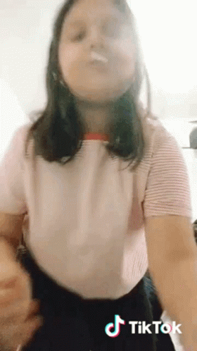 A Girl In A Pink Shirt And Black Skirt Is Making A Tik Tok Video . GIF