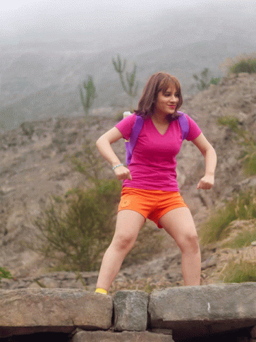 A Girl In A Pink Shirt And Orange Shorts Is Jumping On A Rock GIF