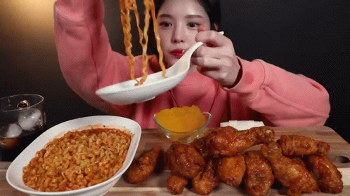 A Girl In A Pink Sweatshirt Is Eating Noodles And Chicken GIF