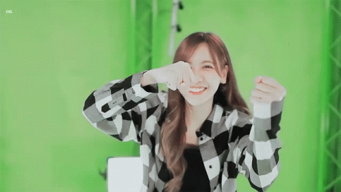 A Girl In A Plaid Shirt Is Smiling And Making A Heart Shape With Her Hands GIF