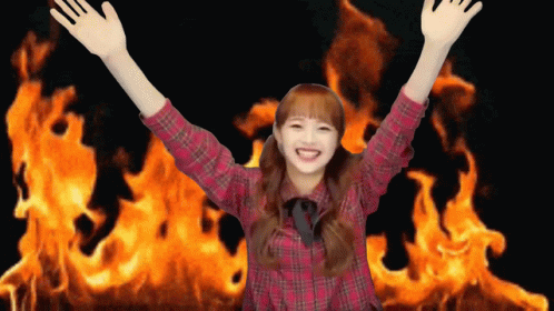 A Girl In A Plaid Shirt Is Standing In Front Of A Large Fire GIF