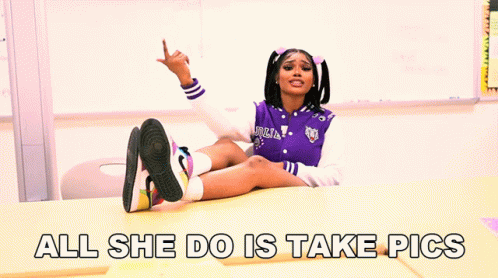 A Girl In A Purple Jacket Sits At A Desk With The Words All She Do Is Take Pics GIF