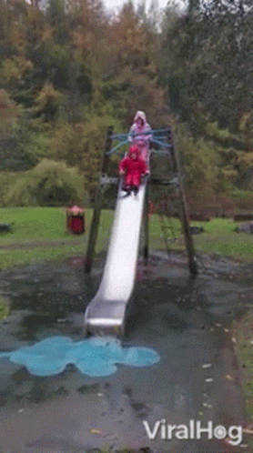 A Girl In A Red Raincoat Is Laying On The Ground In Front Of A Slide In A Park .. GIF
