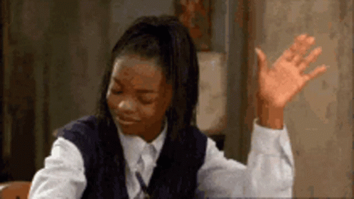 A Girl In A School Uniform Is Sitting At A Desk With Her Hand Up In The Air . GIF