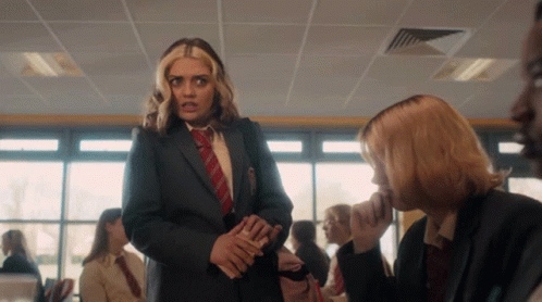 A Girl In A Suit And Tie Talks To Another Girl In A Classroom GIF