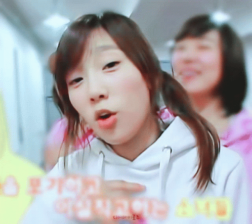 A Girl In A White Hoodie Is Making A Funny Face In Front Of Another Girl GIF
