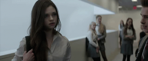 A Girl In A White Shirt Stands In A Hallway With Other People GIF