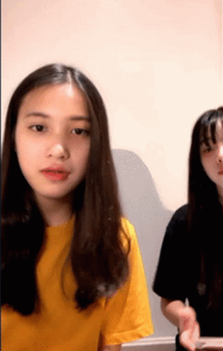 A Girl In A Yellow Shirt Is Sitting Next To Another Girl In A Black Shirt GIF