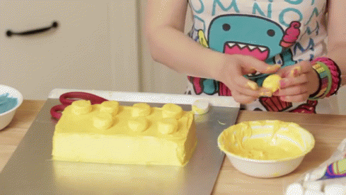 A Girl Is Decorating A Cake With Yellow Frosting GIF