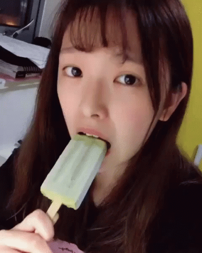 A Girl Is Eating An Ice Cream Bar With A Green Flavor GIF