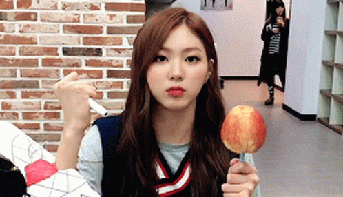 A Girl Is Holding An Apple On A Stick In Front Of A Brick Wall .. GIF