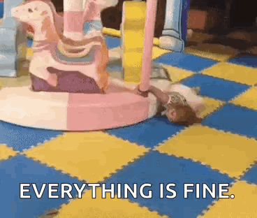 A Girl Is Laying On The Floor In Front Of A Merry Go Round And Says Everything Is Fine . GIF