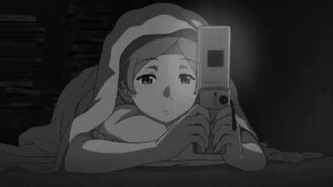 a girl is laying under a blanket holding a cell phone .