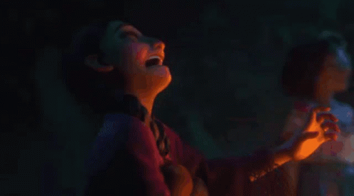 A Girl Is Looking At A Lit Candle In A Dark Room GIF