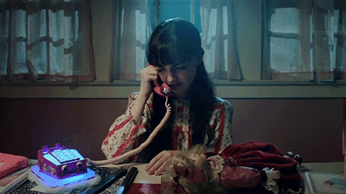 A Girl Is Sitting At A Desk Talking On A Telephone GIF
