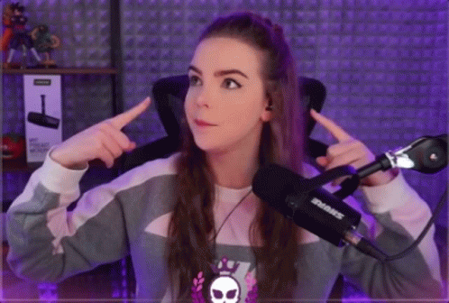 a girl is sitting in front of a shure microphone and pointing at herself .