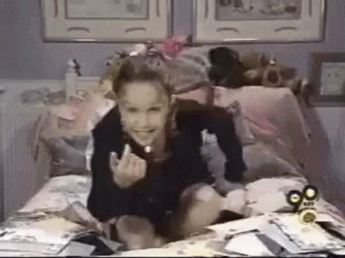 A Girl Is Sitting On A Bed With A 90.Com Logo On The Corner GIF