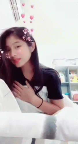 A Girl Is Sitting On A Chair With Her Hands On Her Chest GIF