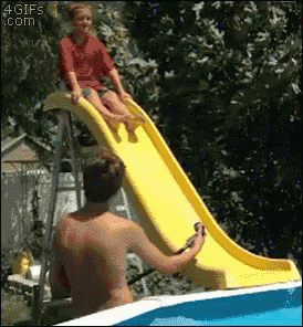 A Girl Is Sitting On A Yellow Slide In A Pool While A Man Watches GIF