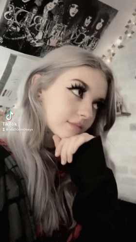A Girl Is Taking A Selfie With A Kiss Poster Behind Her GIF