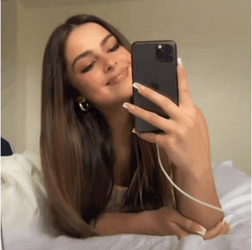 A Girl Is Taking A Selfie With Her Phone While Laying On A Bed . GIF