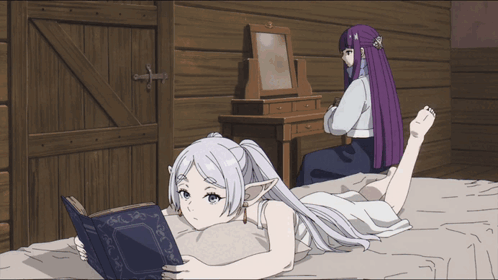 a girl laying on a bed reading a book while another girl sits in the background