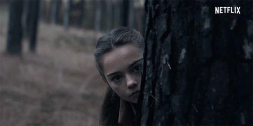 A Girl Peeking Out From Behind A Tree With The Netflix Logo In The Background GIF