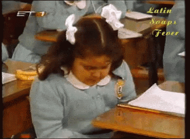 a girl sits at a desk in a classroom with latin soaps fever written on the bottom right