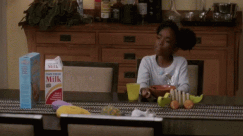 A Girl Sits At A Table With A Box Of Milk And Cereal GIF