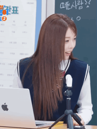 A Girl Sitting At A Desk With An Apple Laptop And A Microphone GIF