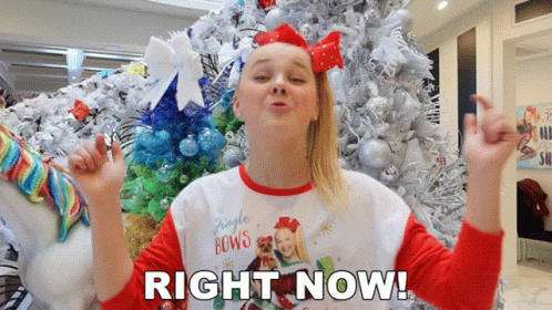 A Girl Standing In Front Of A Christmas Tree With The Words Right Now Written Below Her GIF