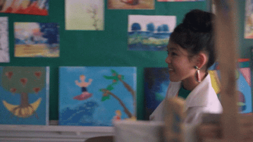 A Girl Stands In Front Of A Wall Of Paintings GIF