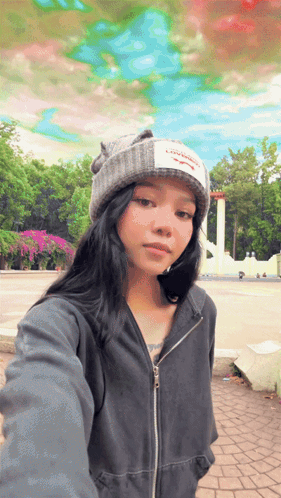 A Girl Wearing A Beanie And A Jacket Taking A Selfie GIF