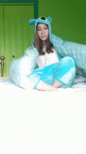 a girl wearing a blue hat and a blue blanket is sitting on a bed
