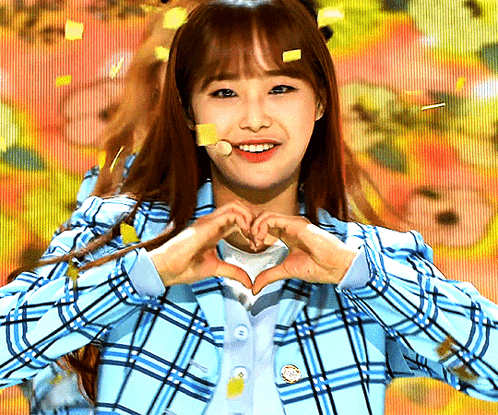 A Girl Wearing A Blue Plaid Jacket Making A Heart Shape With Her Hands GIF