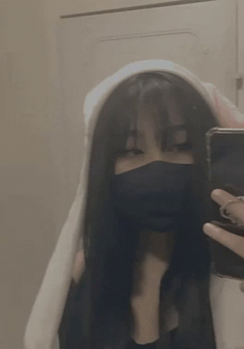 A Girl Wearing A Mask And A Hoodie Is Taking A Selfie With Her Phone . GIF