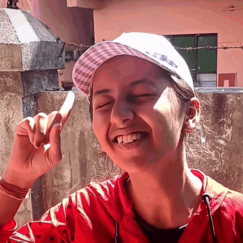 A Girl Wearing A Red Jacket And A White Hat Is Smiling GIF