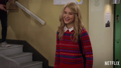 Girl In Red Sweater Smiling In Front Of Netflix Sign GIF