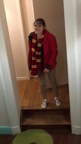 A Girl Wearing A Scarf And A Red Jacket Stands In A Hallway GIF