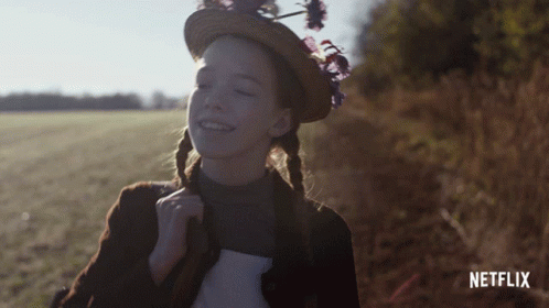 A Girl Wearing A Straw Hat With Flowers On It Is Smiling In Front Of A Netflix Logo GIF