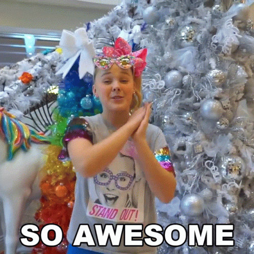 A Girl Wearing A T-Shirt That Says " Stand Out " Is Clapping In Front Of A Christmas Tree GIF