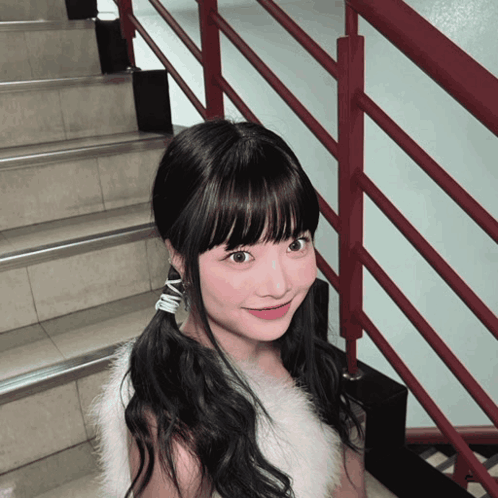 A Girl Wearing A White Fur Vest And Earrings With The Letter N On Them GIF