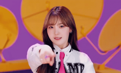 A Girl Wearing A White Jacket And A Pink Tie Points At The Camera . GIF