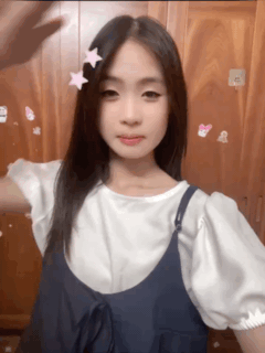 A Girl Wearing A White Shirt And Blue Overalls Has A Pink Star In Her Hair GIF