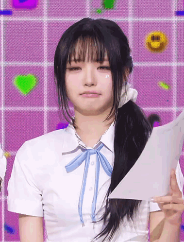 A Girl Wearing A White Shirt With A Blue Bow Tie Holds A Piece Of Paper GIF